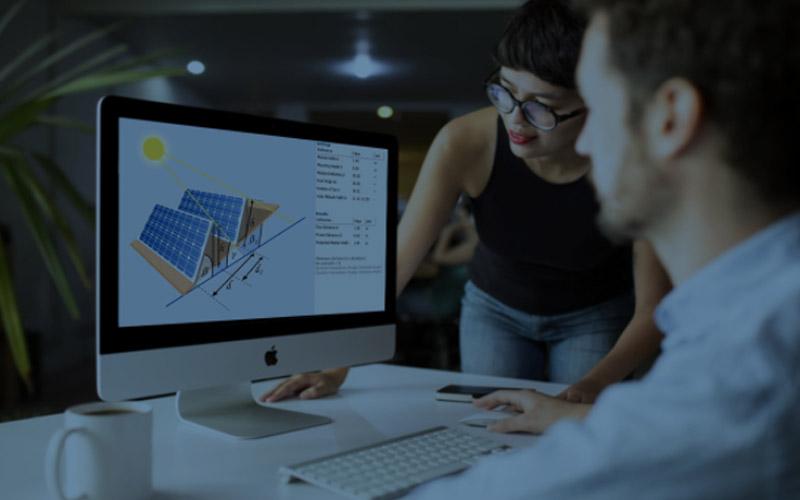 Two people working at computer monitor with solar panel graphics on screen